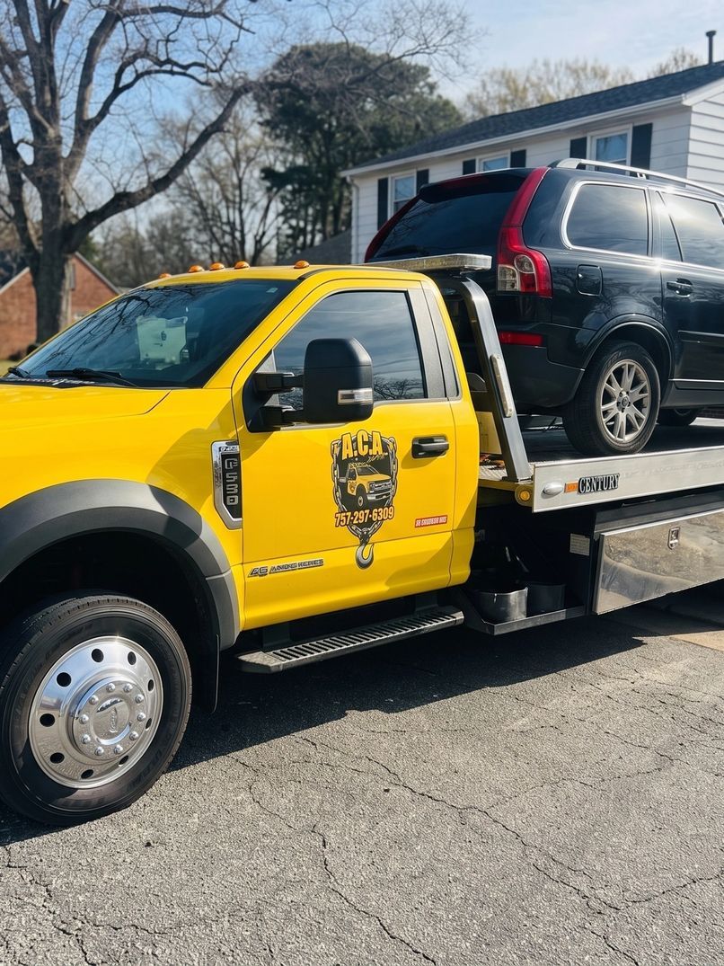 A.C.A. yellow flatbed tow truck carrying a black SUV